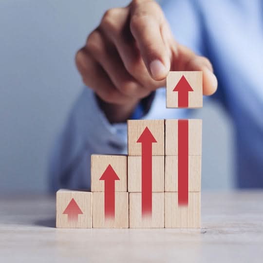 Hand placing a wooden block with a red arrow on top of a stack of similar blocks. Growth Package