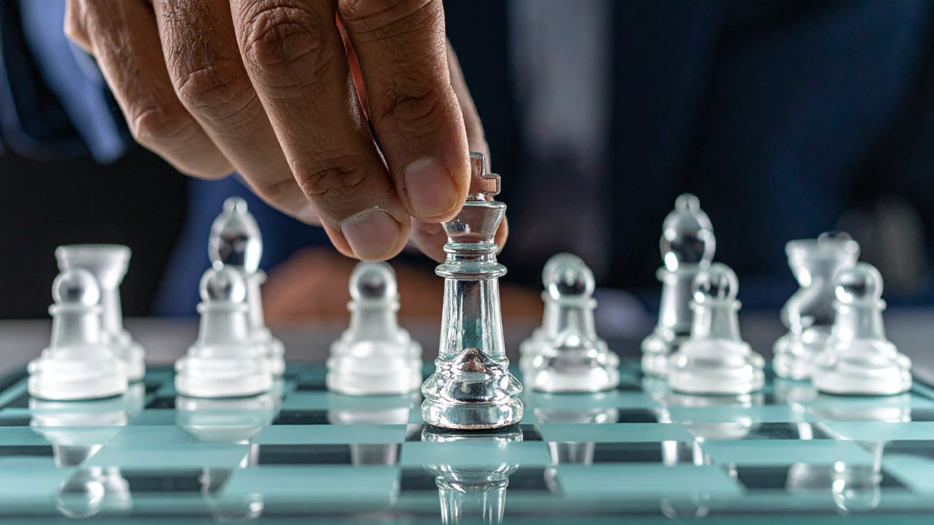 Hand moving a chess piece on a glass chessboard